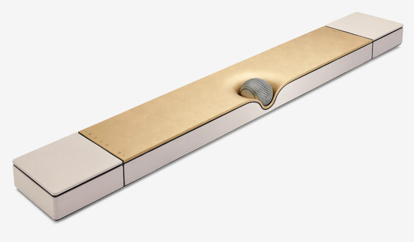 Angled top view of special edition Devialet Dione Opéra de Paris soundbar, with spherical center speaker in the front center and gold leaf covered top, with two up-firing Dolby Atmos drivers on each end of the soundbar.