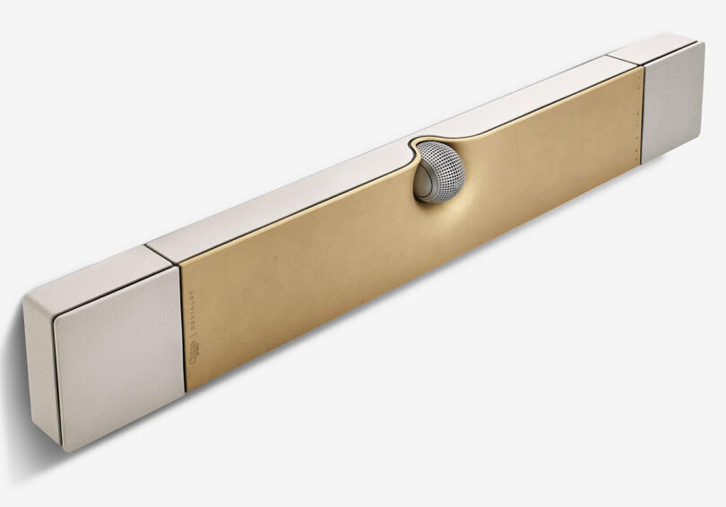 Angled view of special edition Devialet Dione Opéra de Paris soundbar, with spherical center speaker in the front center and gold leaf covered top, with two up-firing Dolby Atmos drivers on each end of the soundbar.