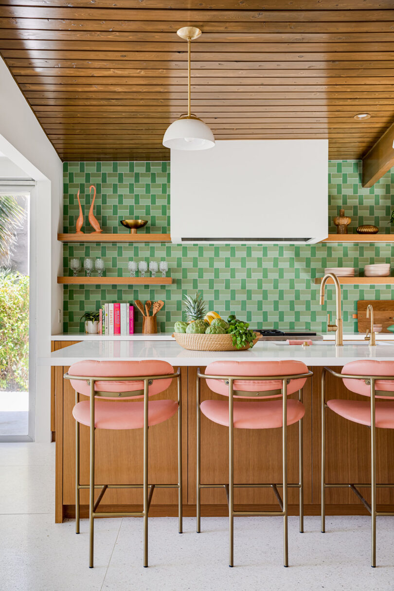 colorful kitchen with light green backsplash, pink counter stools, and open wood shelving