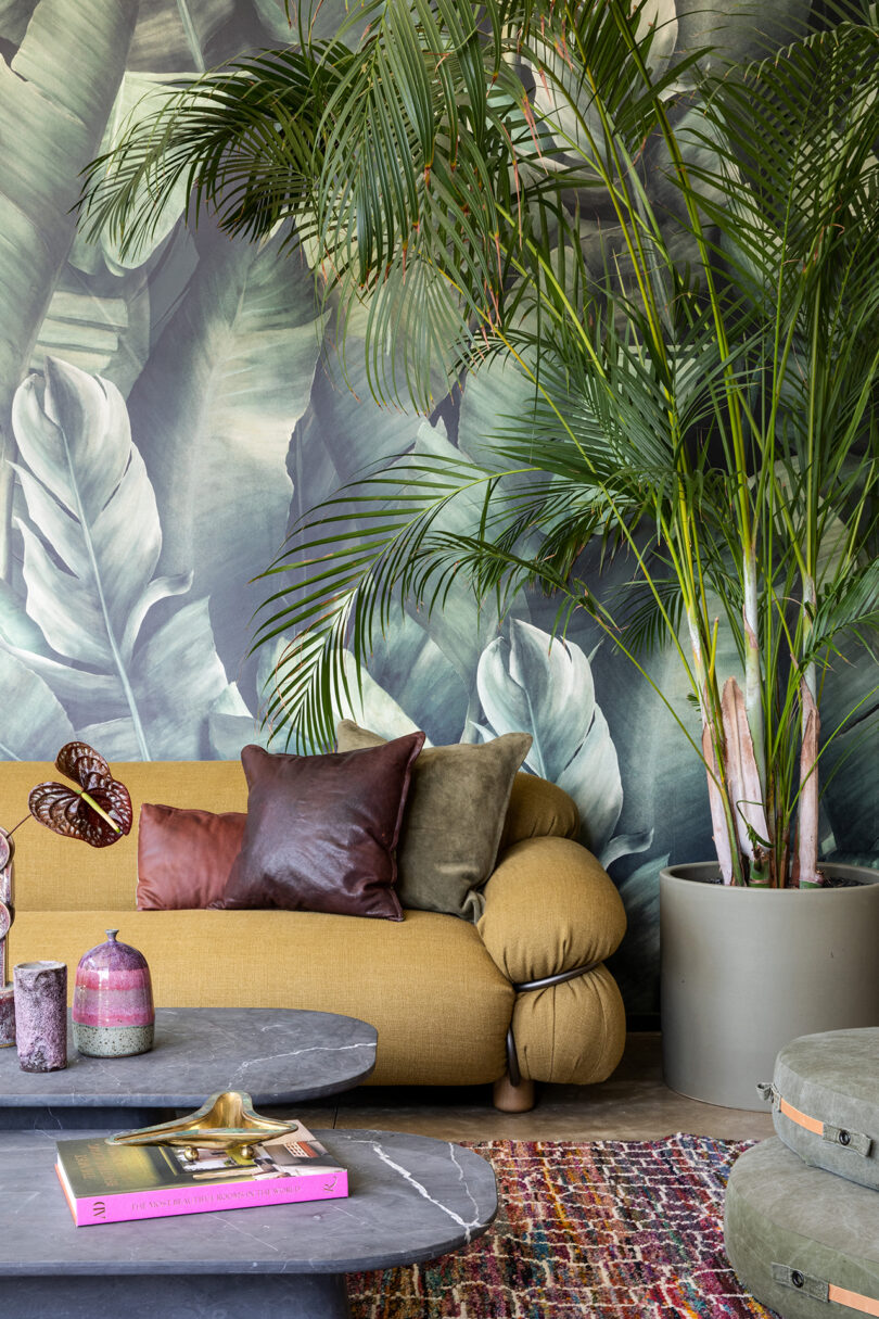 colorful living space with ochre sofa, tall floor plant, and palm leaf wallpaper