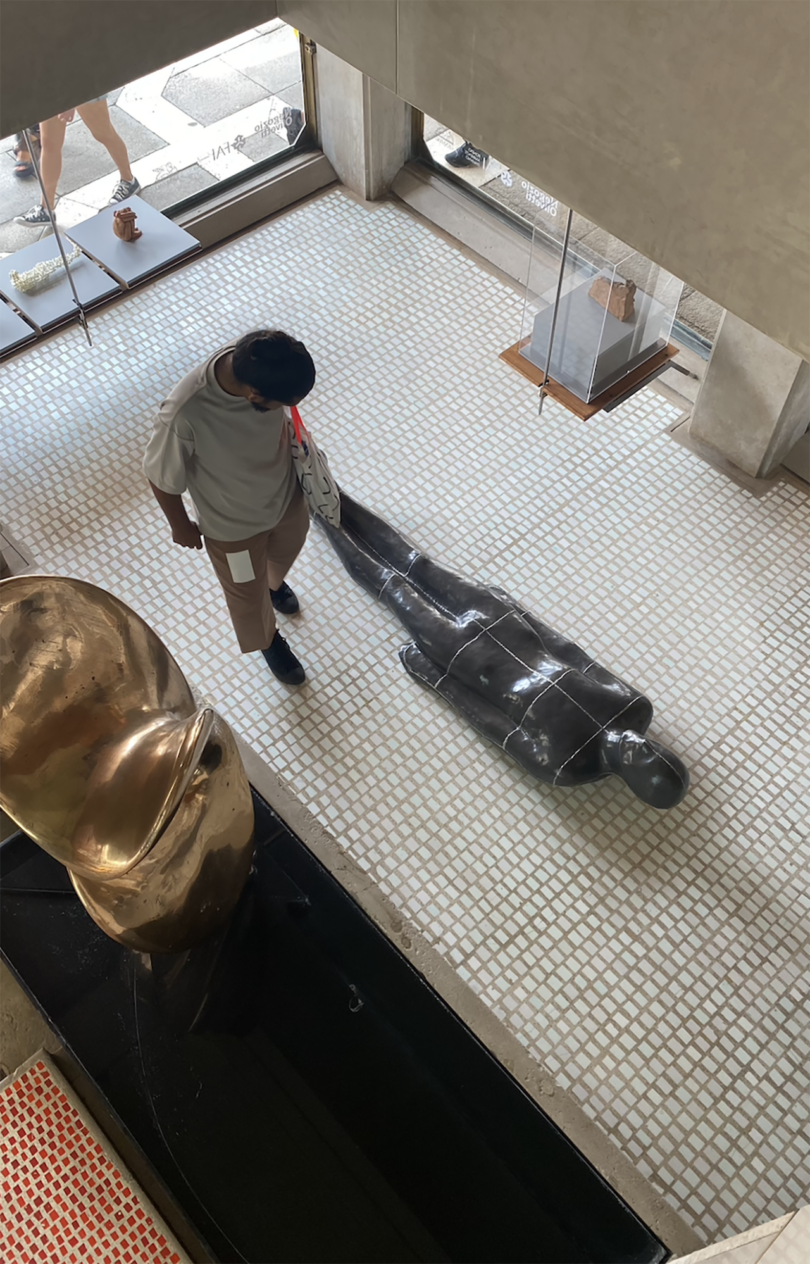 overhead photo of a light-skinned person observing a human-shaped sculpture