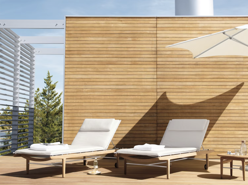 two outdoor chaise lounges with white cushions in front of a modern wood privacy fence