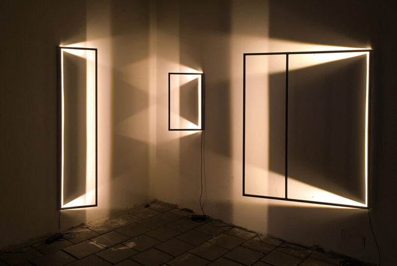 three wall lights that appear to be suspended inside thing frames