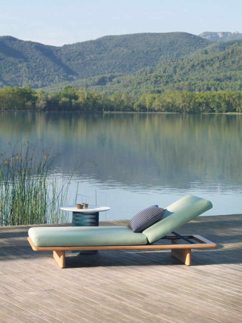 wood chaise lounge with seafoam cushions next to a body of water