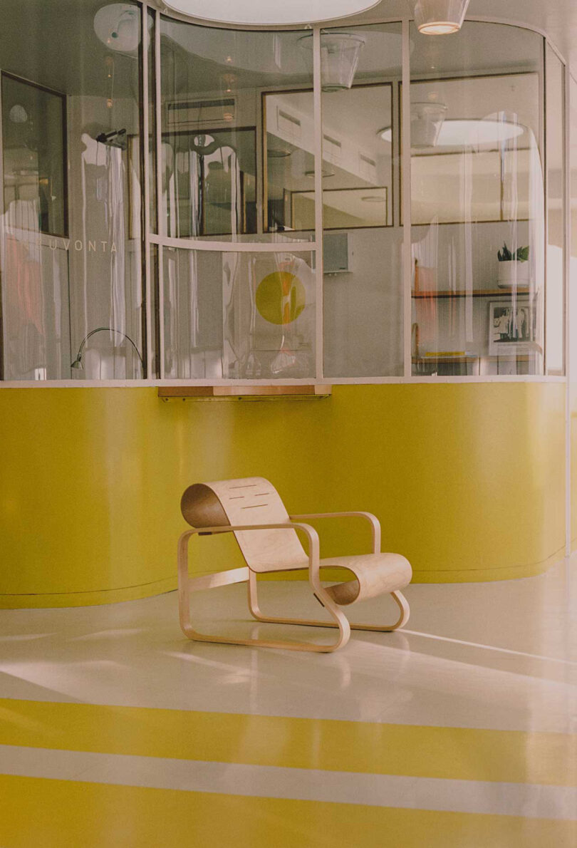 poltrona de madeira curvada em frente à área de recepção em amarelo neon e branco, atrás de um vidro