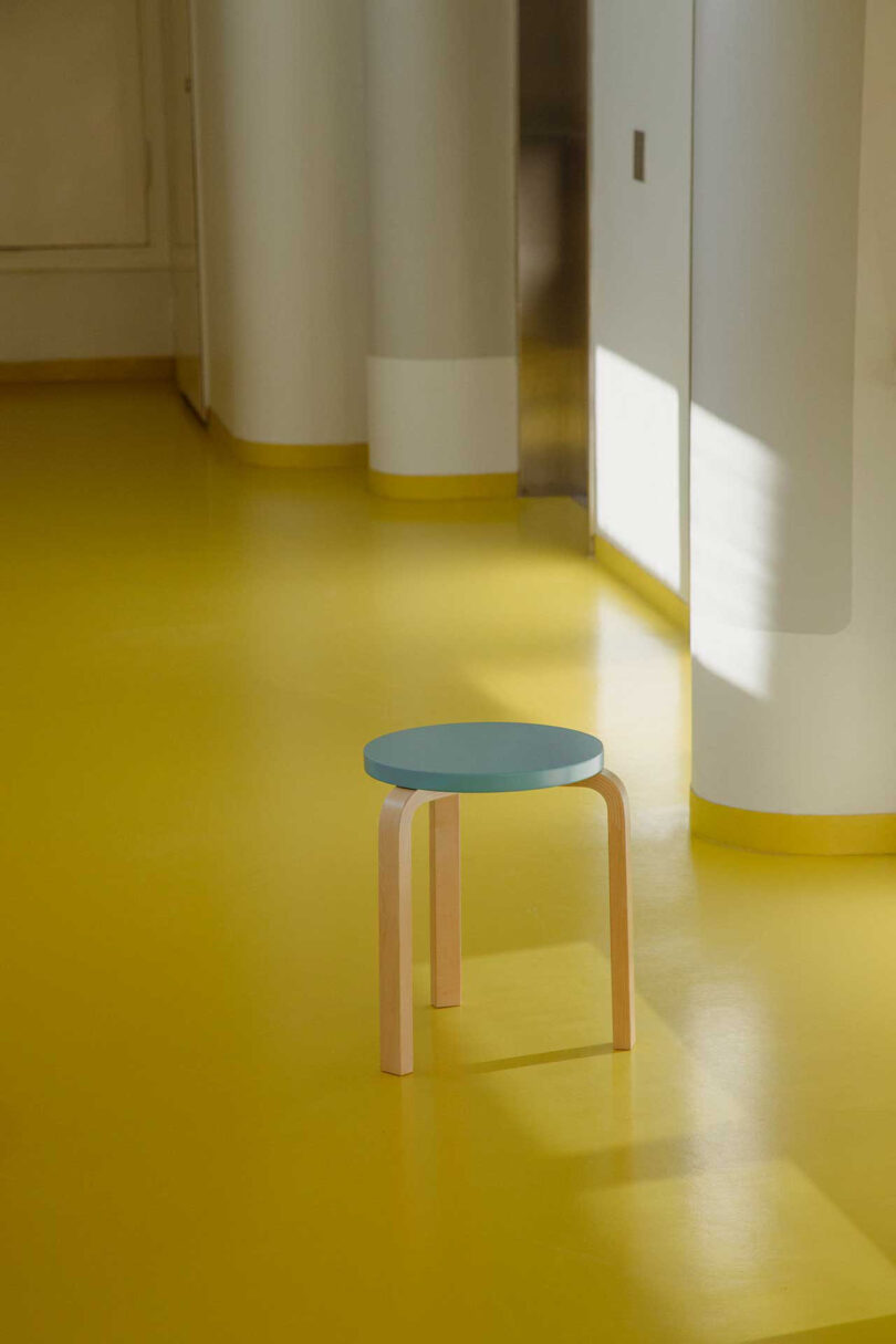 banquinho de três pernas com assento azul claro em espaço com piso amarelo