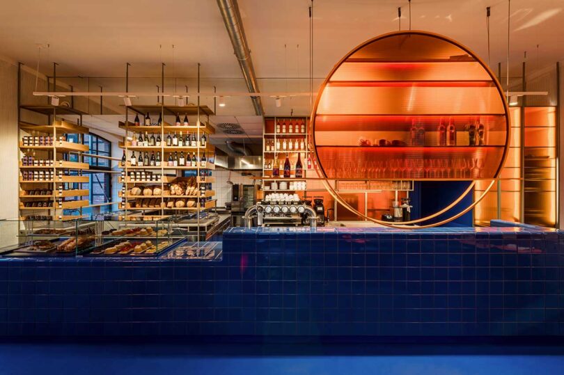 evening view of commercial restaurant interior with modern aesthetic featuring blue tiled counter and pastries stacked on shelving
