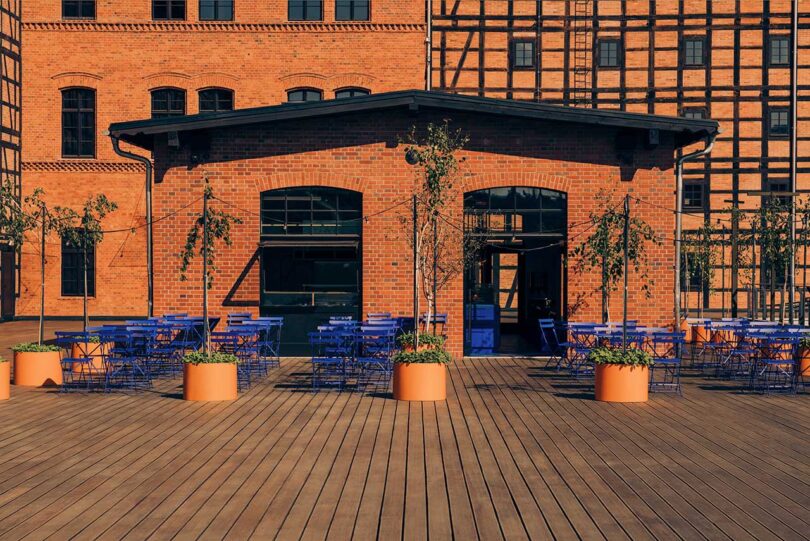 exterior shot of brick industrial building with blue chairs on patio