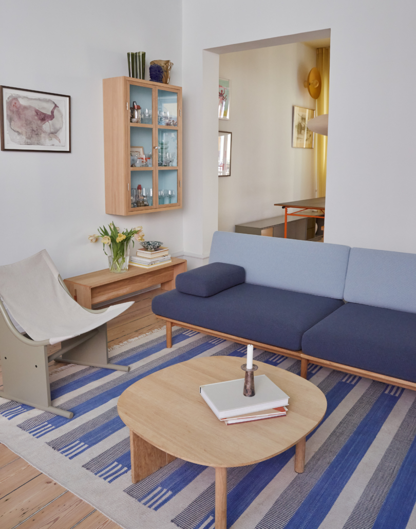 A room with an architectural armchair, a wooden coffee table and the spoke sofa upholstered in two shades of grey/blue