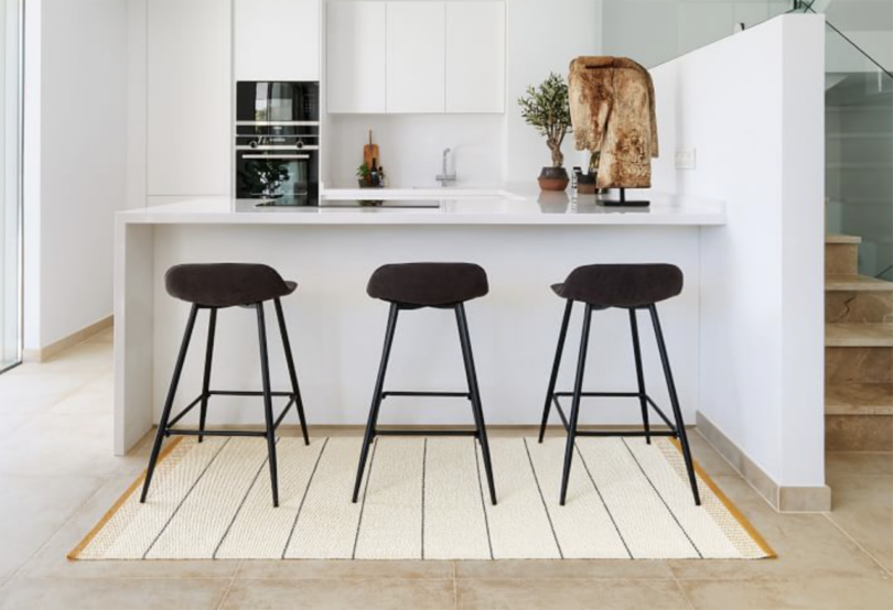 kitchen space with three black counter height stools and a striped rug