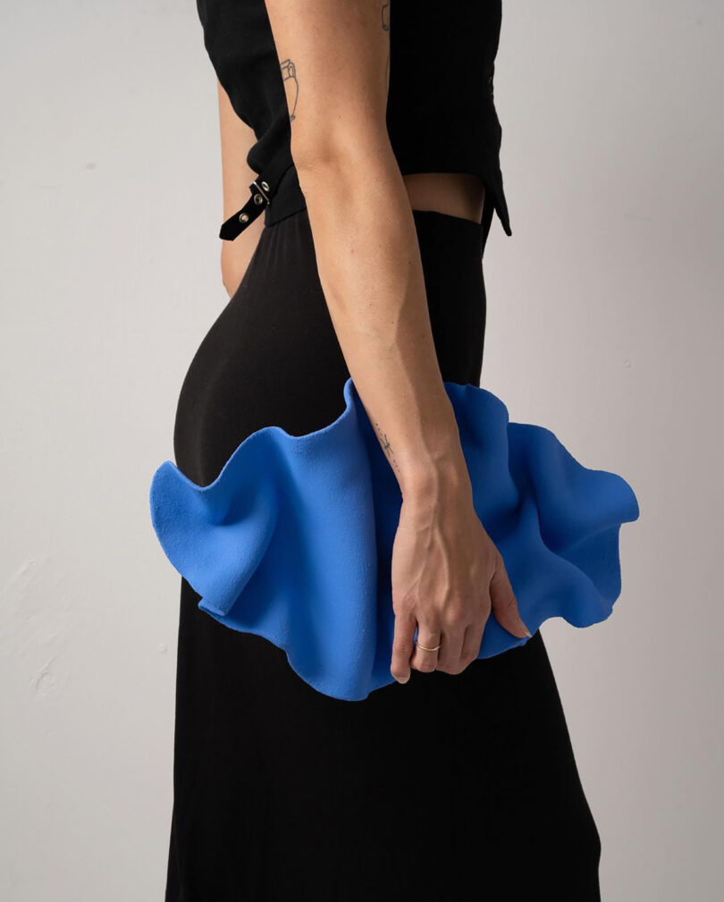 a blue oval-shaped wrinkled clay wall sculpture being held like a purse