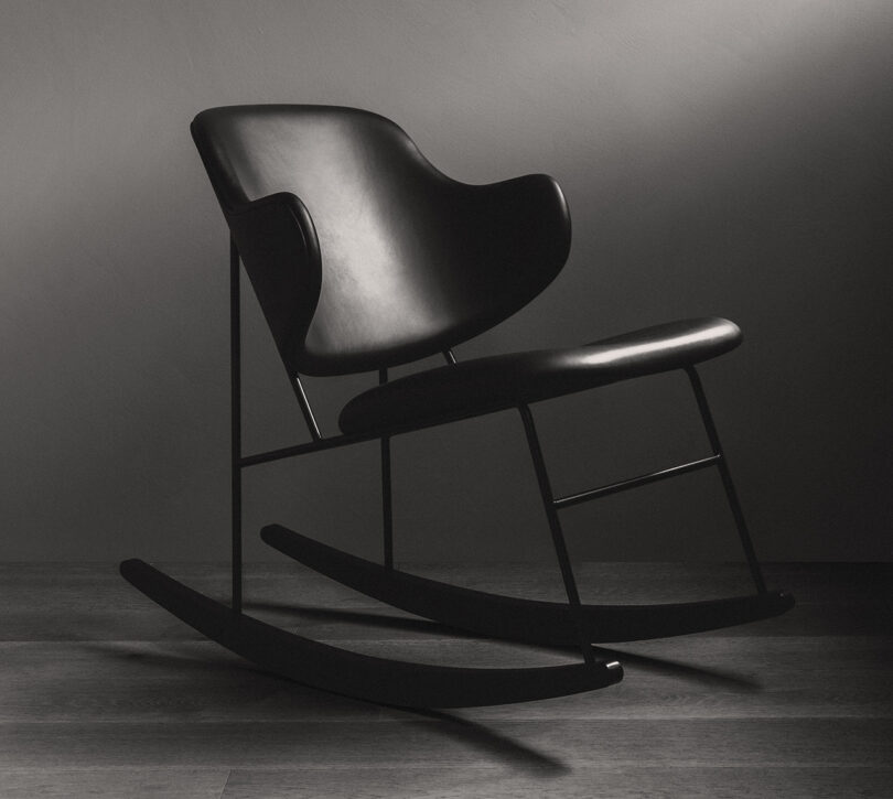 Front angled view of the Penguin Rocking Chair in all black leather seat and back, set in a room with dark gray flooring and walls.