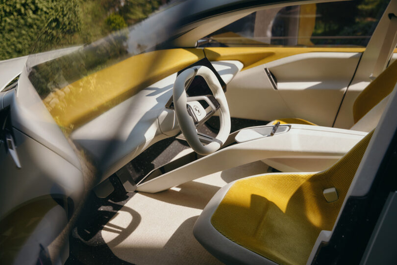 Driver side view of the steering wheel inside the BMW Vision Neue Klasse concept. Interior is yellow across the seats and top of the dash, and an off-white everywhere else across the cabin.