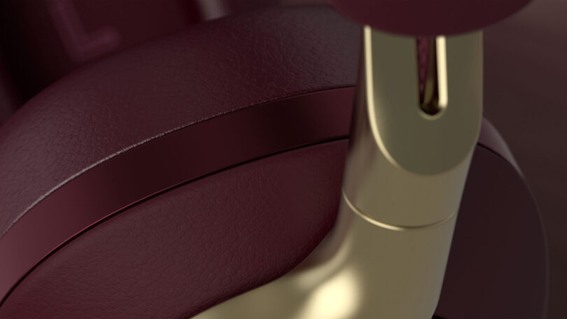 Close up detail of Bowers & Wilkins Px8 in Royal Burgundy Nappa leather finish with gold detailing where the arms meet the ear cups.