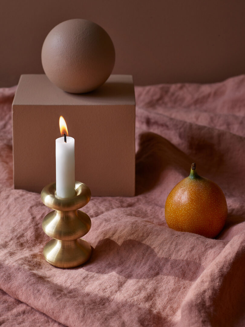 modern brass candle holder with an illuminated white candlestick on a styled surface