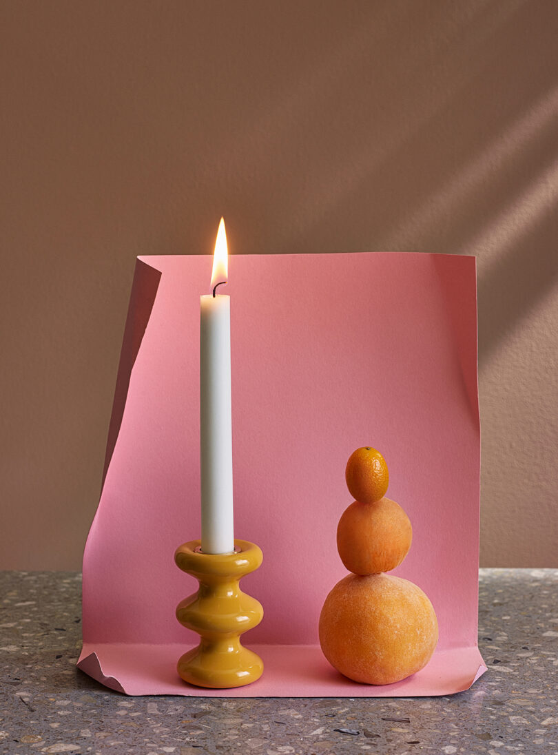 modern orange candle holder with an illuminated white candlestick on a styled surface