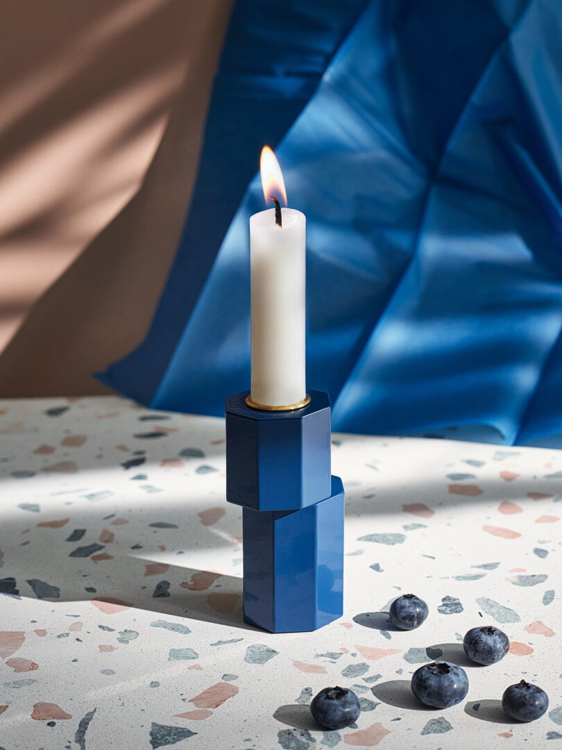 modern blue candle holder with an illuminated white candlestick on a styled surface