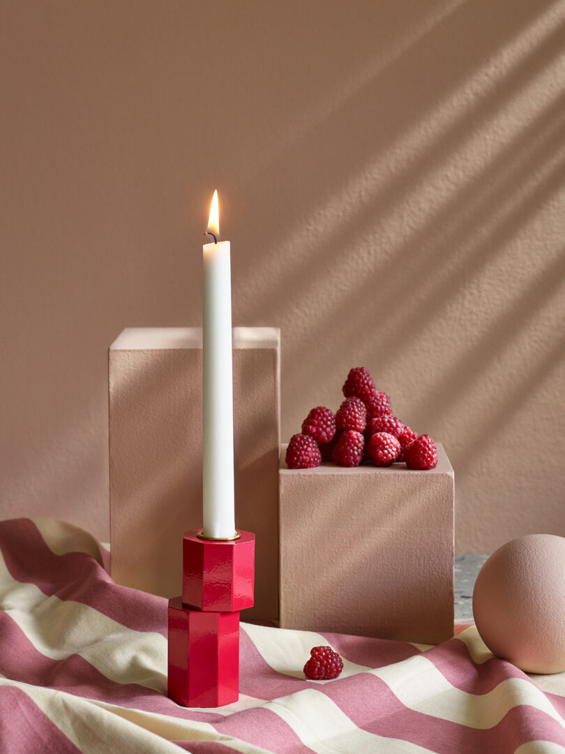 modern red candle holder with an illuminated white candlestick on a styled surface