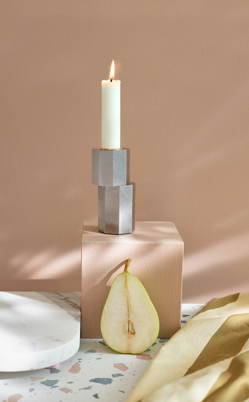 modern silver candle holder with an illuminated white candlestick on a styled surface