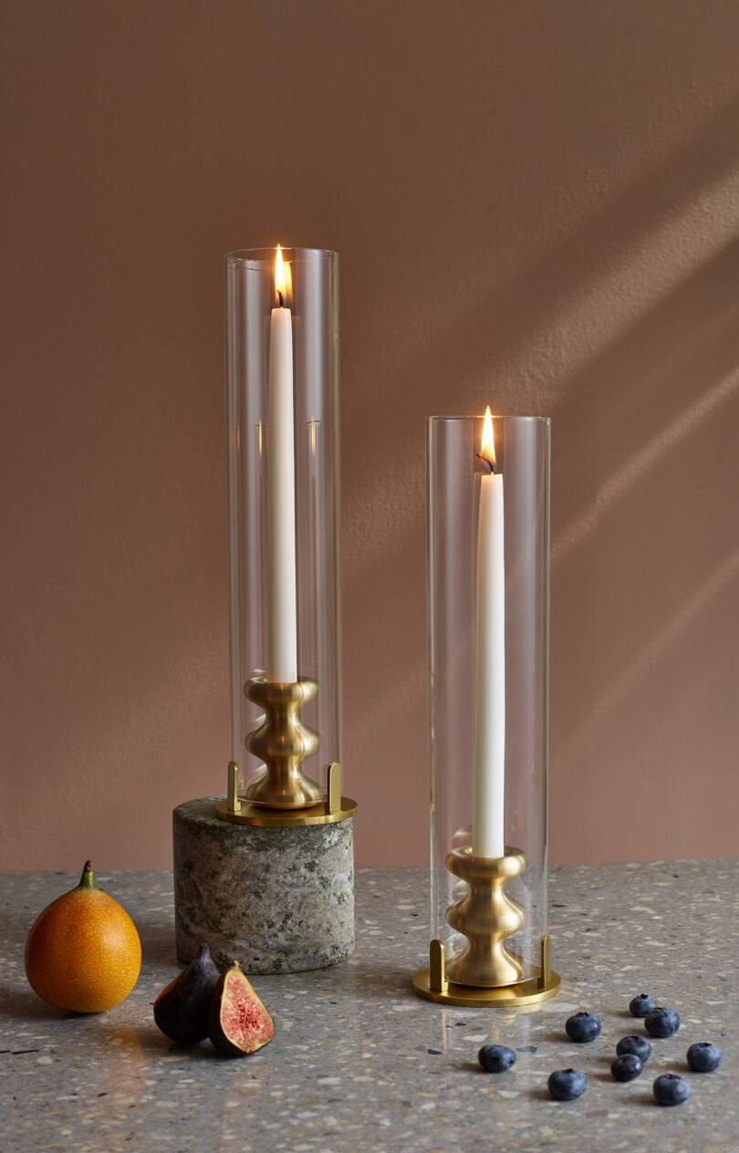 two modern brass candle holders with glass covers and illuminated white candlesticks on a styled surface