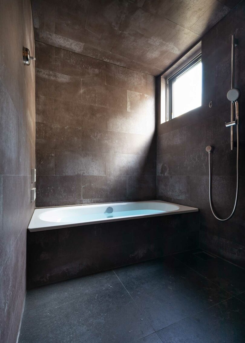 view into modern bathroom with dark moody tiles and walls