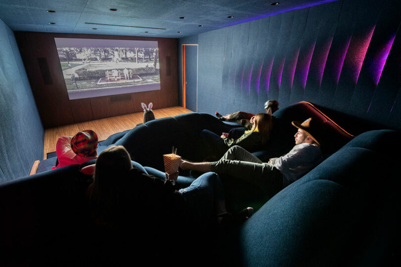 angled back view of home theater with wave-like dark blue seating with people sitting randomly