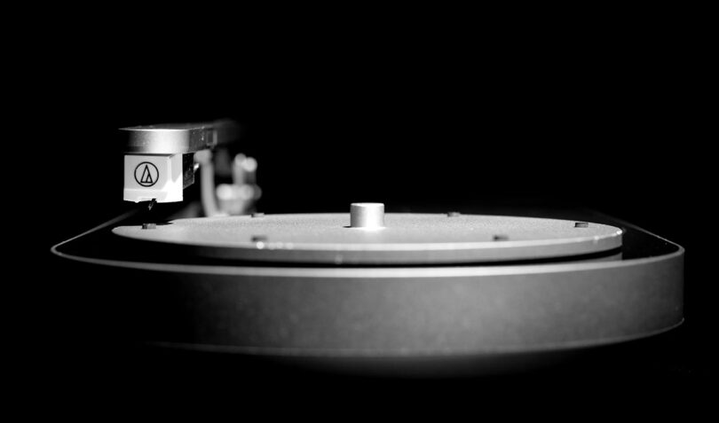 Side eye level perspective of Coturn record player in black and white photo, with detailed shot of tone arm and needle.