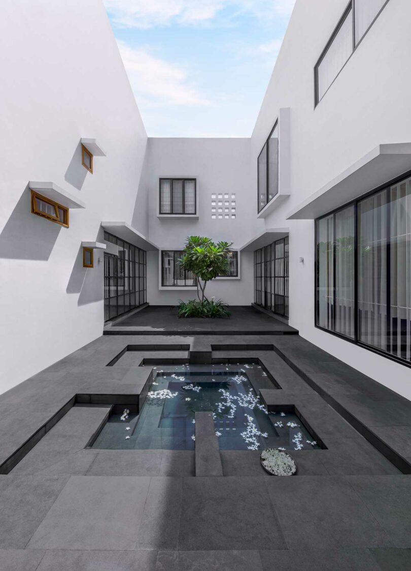 Exterior shot of wrap around white house with geometric black floored courtyard with geometric water feature