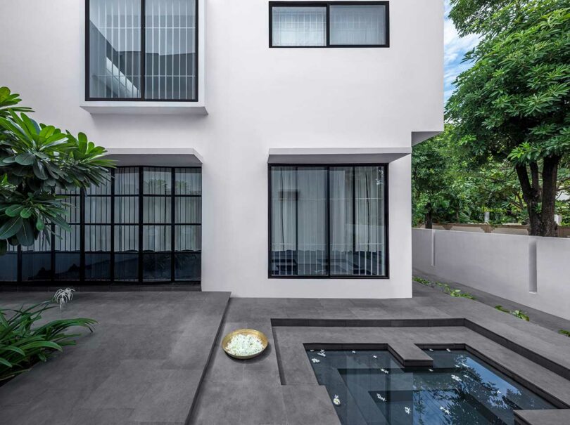 partial exterior shot of white house with black framed windows and black floored courtyard with geometric water feature