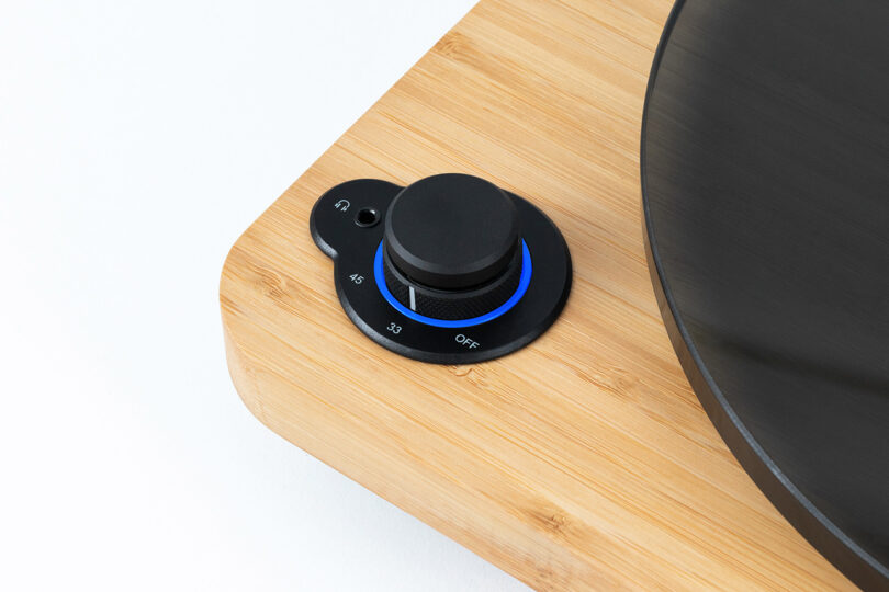 Detail of Stir It Up Lux's knurled dial controls with glowing blue light and 45, 33, and Off settings printed across its diameter. Dial is set to 33. Small headphone port is to the left side, with turntable platter partially visible.