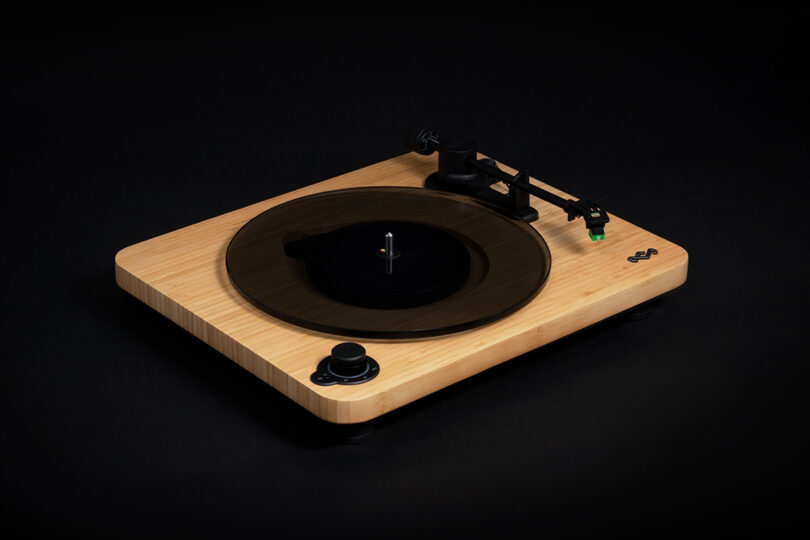 House of Marley's Stir it Up Lux Bluetooth Turntable with bamboo plinth and dark glass platter and green tipped record needle cartridge, with all-black background.