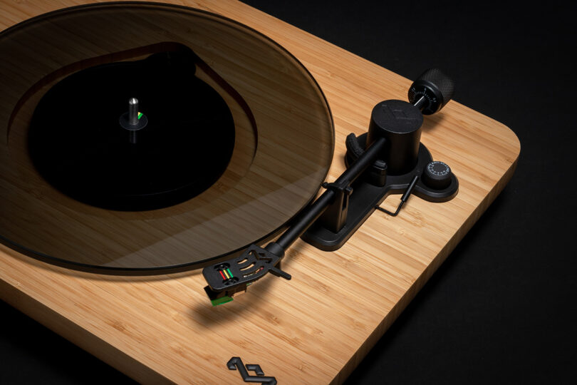 Cropped right side of House of Marley's Stir it Up Lux Bluetooth Turntable with bamboo plinth and dark glass platter and Jamaican color tipped record needle cartridge, with all-black background.