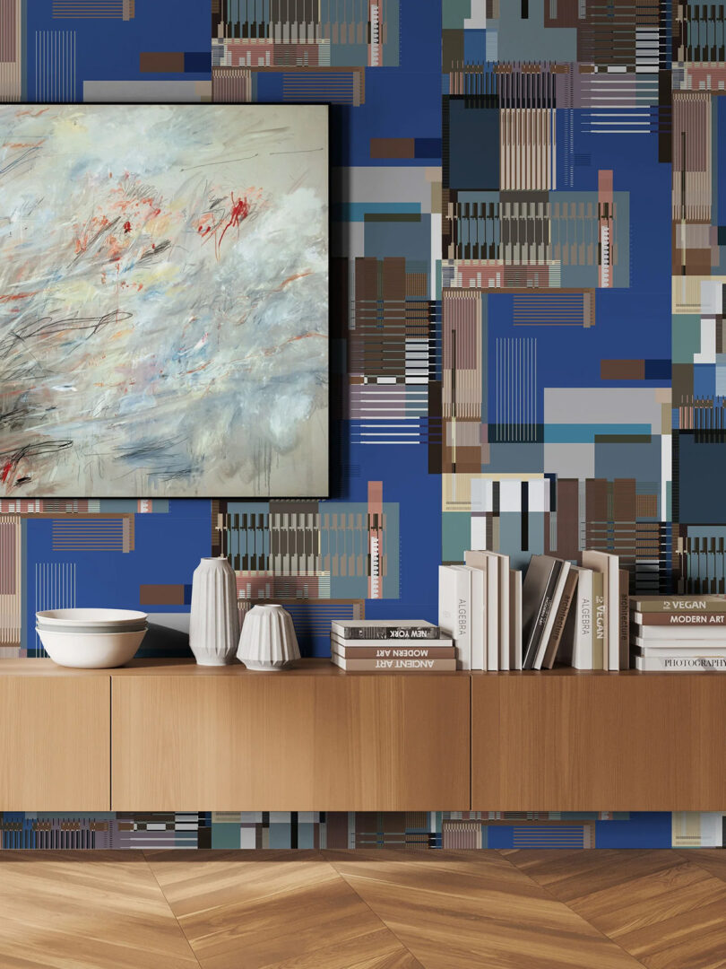 Jupiter 10 Glitch blue wallpaper staged in living room with long wood console in background underneath wallpaper installation; ceramic bowls, vases and books staged across console, artwork to the left.