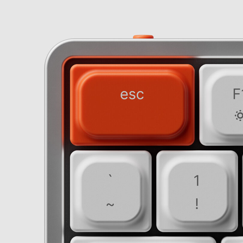 Close up of ESC key in orange located in the upper left hand corner of a mechanical keyboard. Surrounding keycaps are white.