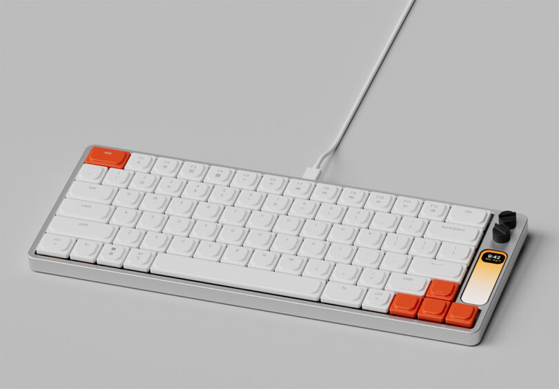 Angled full size image of The Knob keyboard connected by USB-C. Upper right hand ESC key and four arrow keys are in orange, rest of the keycaps are all white, with two black rotary knobs in the upper right hand corner of the keyboard.