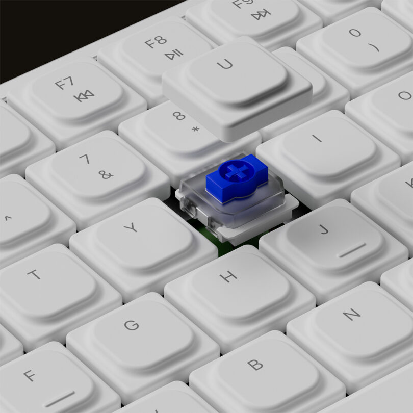 Close-up of exposed mechanical Blue Gateron switch in the middle of white keycaps.