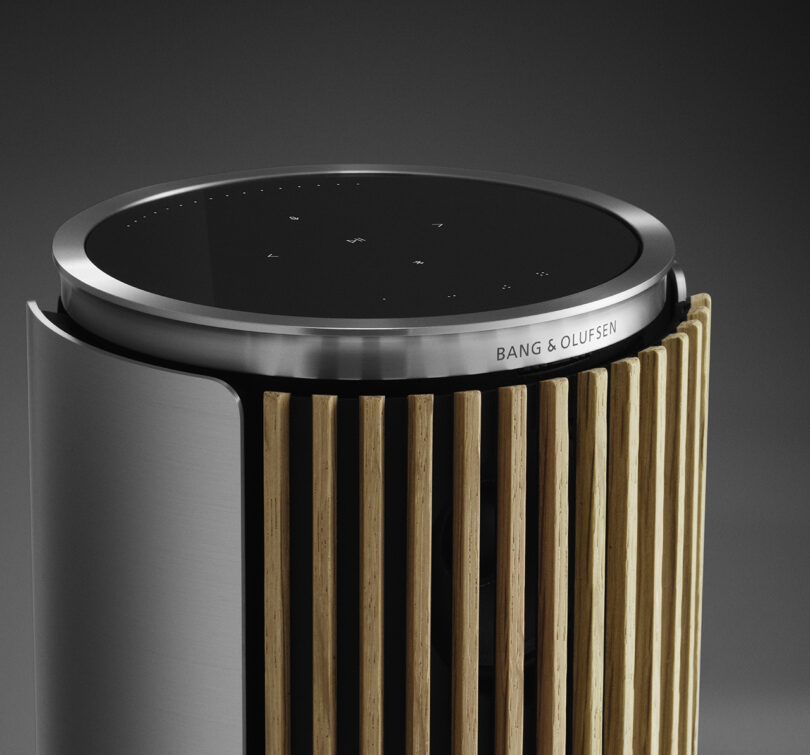 Close up of the upper half of the slatted wood cover of the Beolab 8 wireless speaker, showing its black glass touch control interface.
