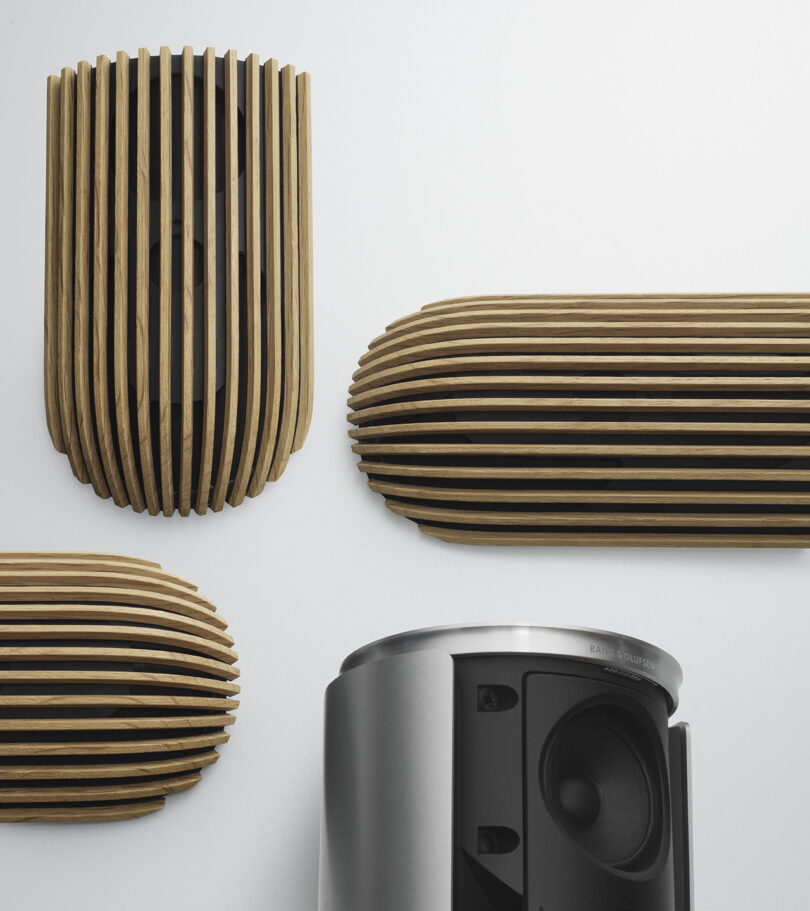 Three sets of slat wood covers removed from the Beolab 8, with one aluminum speaker base placed nearby showcasing its one-piece aluminum base design and speaker.