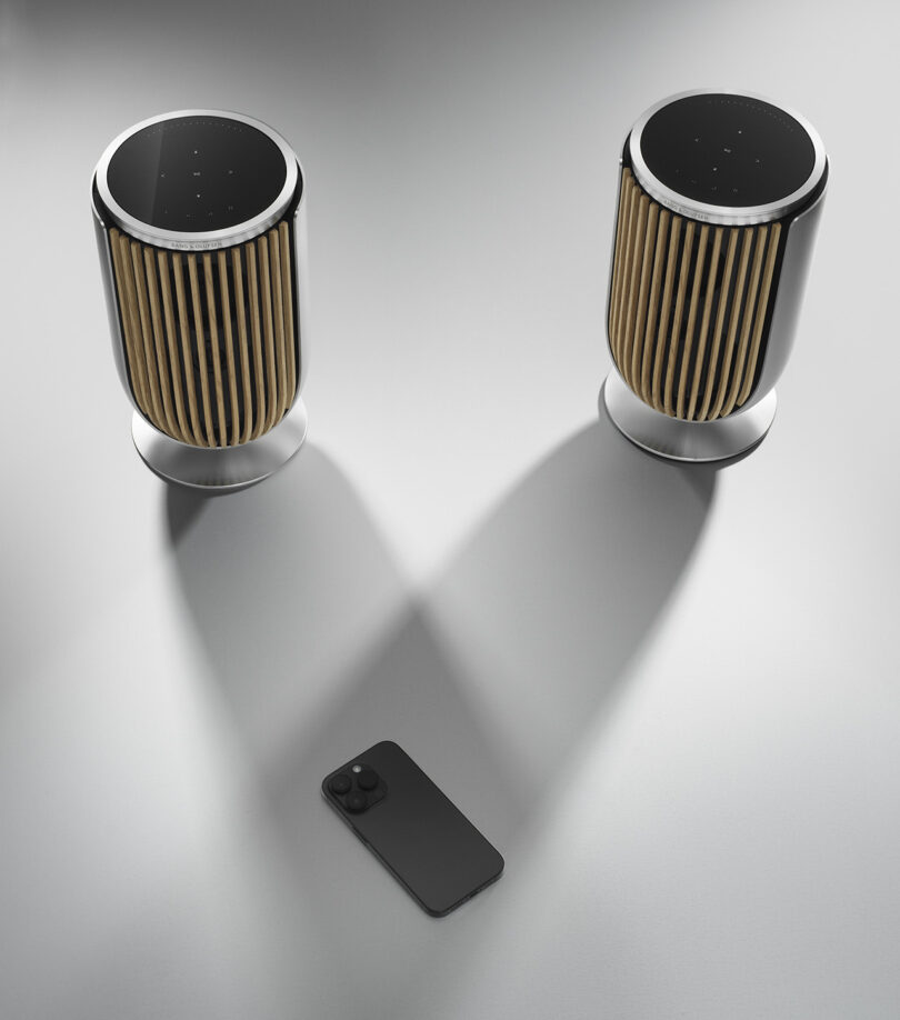 Two Beolab 8 speakers shown with one iPhone, illustrating the speaker's stereo mode features.