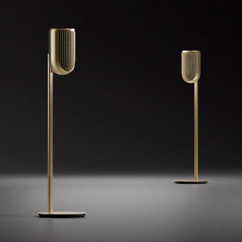 A pair of Beolab 8 speakers in gold, set on matching gold stands in a darkened set room.