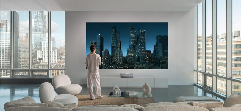 living room scene with floor-to-ceiling windows and man standing in front of projected movie on wall