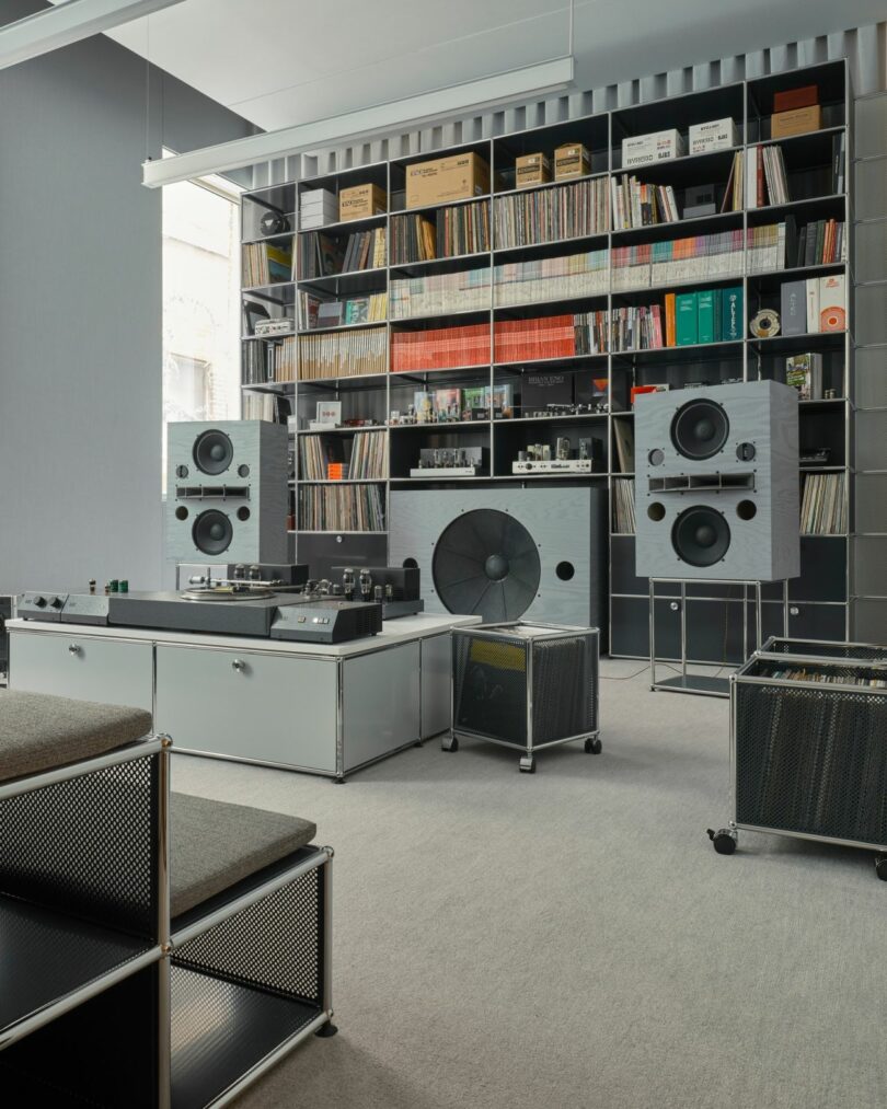 OJAS Listening Room at USM Modular Furniture with large modular bookshelf system filled with books, vinyl records, audio components and other miscellaneous items, with turntable and two tube amps set across a rolling platform storage. Room is decorated in all neutral gray decor.