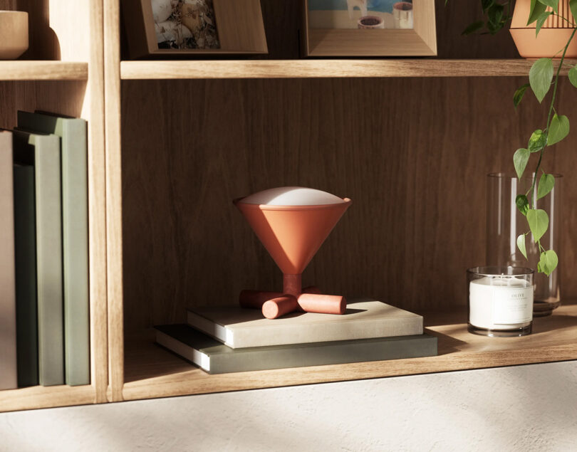 Umbra CONO in Sierra colorway, set on top two books set within a section of floor-height shelves. Candle, houseplant, picture frames, and other books are visible staged around the lamp.