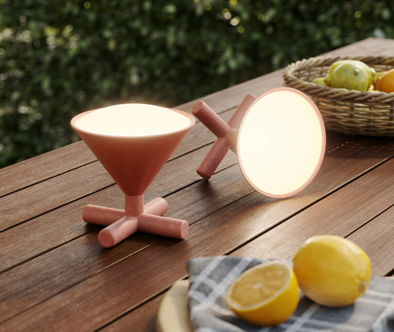 Two Umbra CONO LED lights in Sierra color set across a staged outdoor wood table with lemons in the foreground and basket of other citrus fruit in the background.