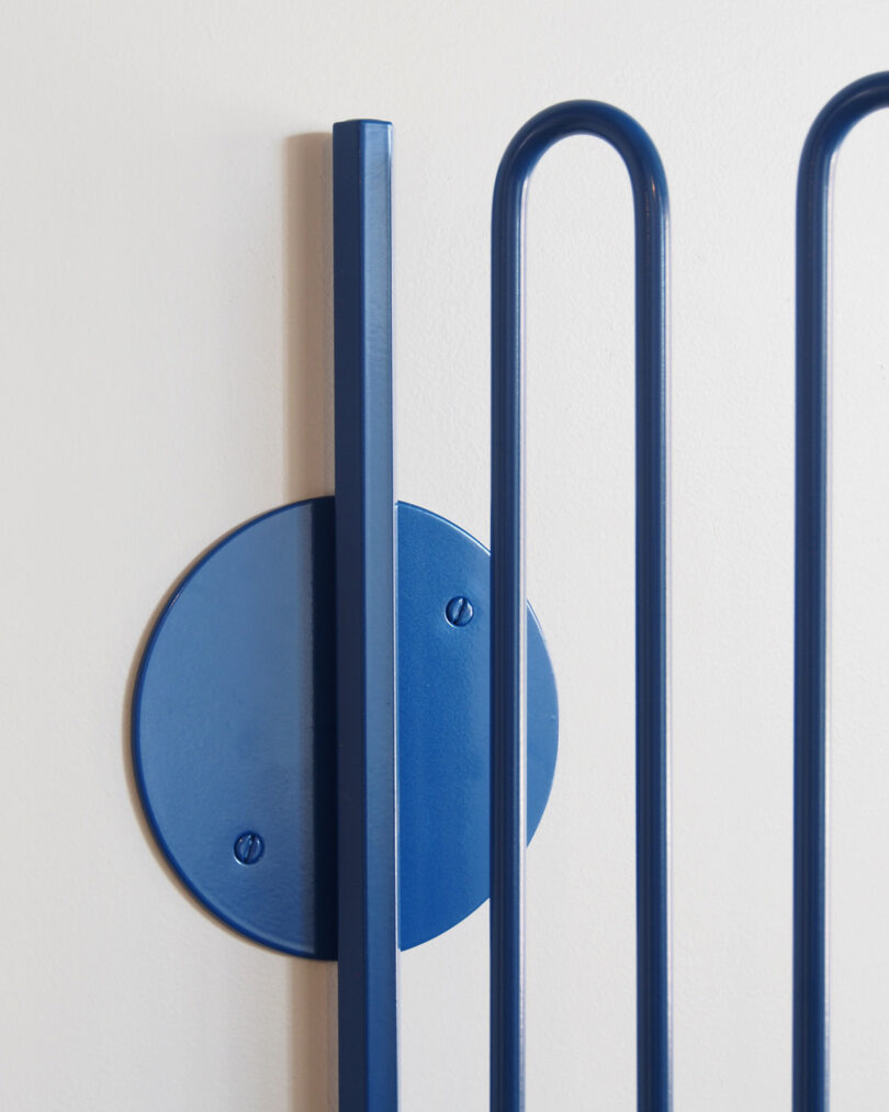Close up of the wavy aluminum blue lamp arm and where it attaches to the wall with a circular base.
