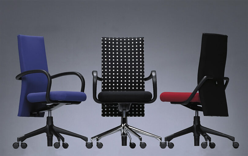 Three Vitra AC1 task chairs in blue, black and white dot pattern, and red upholstery. Both left and right chairs are angled, with center black and white chair facing forward. All three feature caster wheels.
