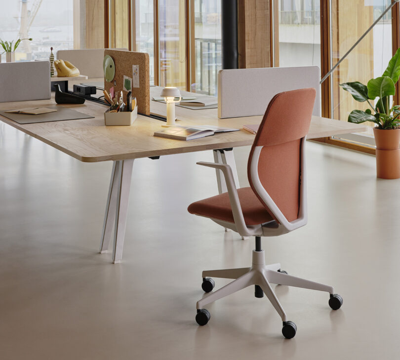 Vitra ACX at the foot of a long conference table accessorized with small privacy partitions and small desk lamp, stationery, and an open book.