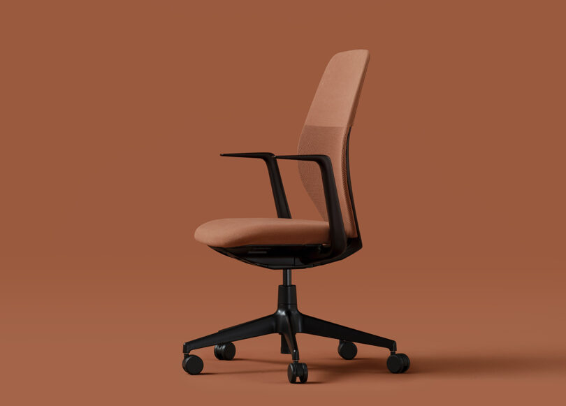 A Vitra ACX task chair against a salmon-orange hued background with black arms and base with caster wheels. Chair is facing toward the left in profile.