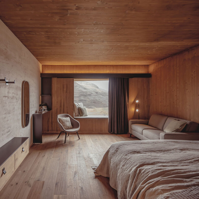 cozy hotel room with wood surfaces and ceilings and neutral tan furnishings with window views of surrounding terrain.