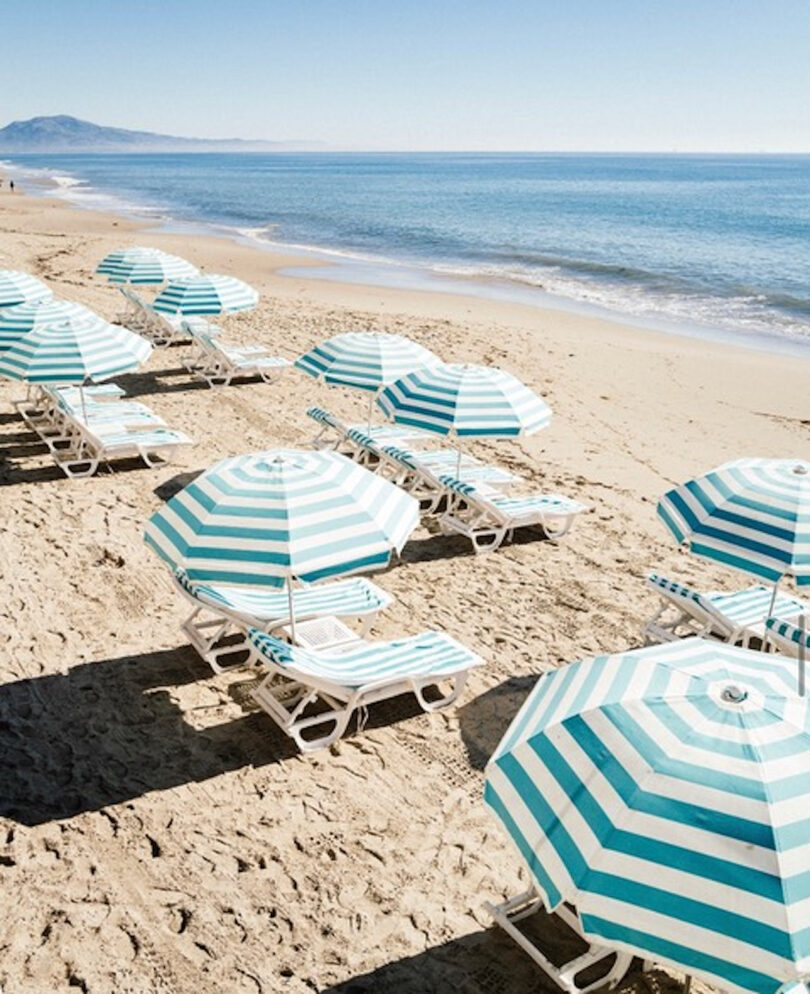 a beach covered in green and white striped umbrellas and folding deck chairs with white cushions